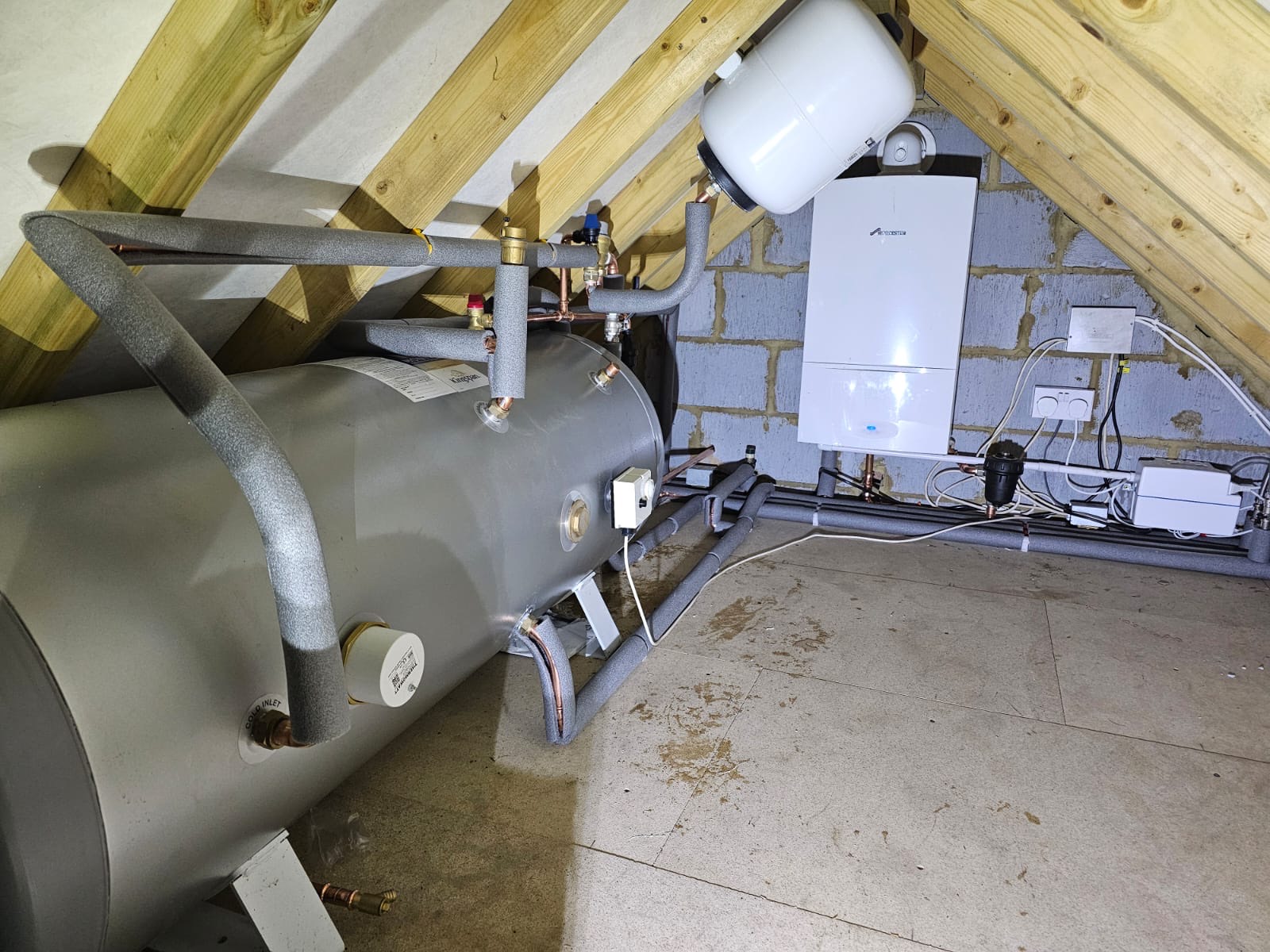 A loft plant space finished off: cylinder, boiler, expansion vessel and controls, with the pipework lagged and clipped.