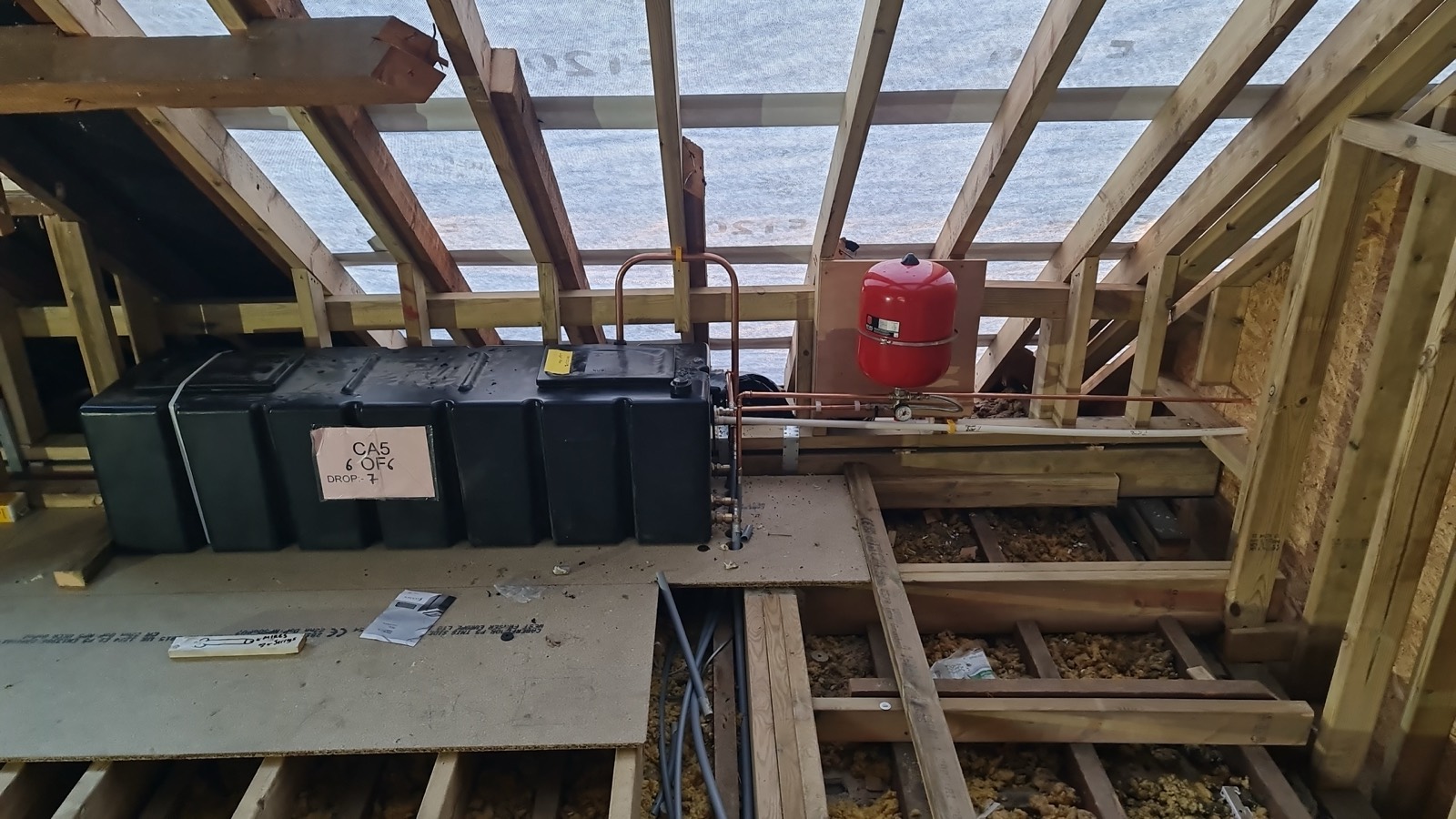 First fix in a loft conversion: expansion vessel mounted, pipe runs set out and tanks positioned before the boarding goes down.